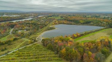 An aerial shot of solar panels among fields and forest.